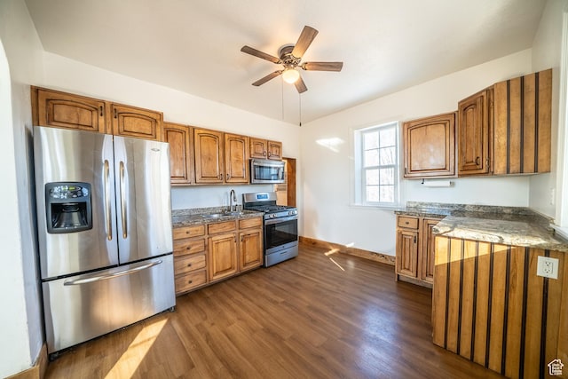 kitchen featuring dark wood-style floors, brown cabinets, appliances with stainless steel finishes, a sink, and ceiling fan