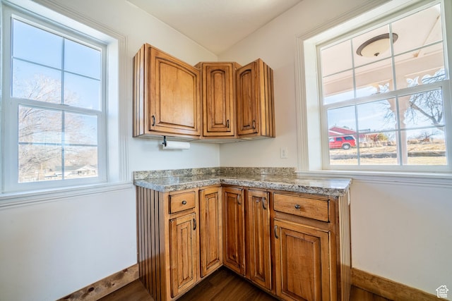 kitchen with brown cabinetry, dark wood-style flooring, light countertops, and baseboards