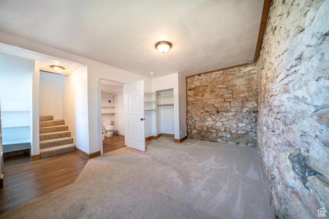 unfurnished bedroom with carpet floors, connected bathroom, baseboards, and a textured ceiling