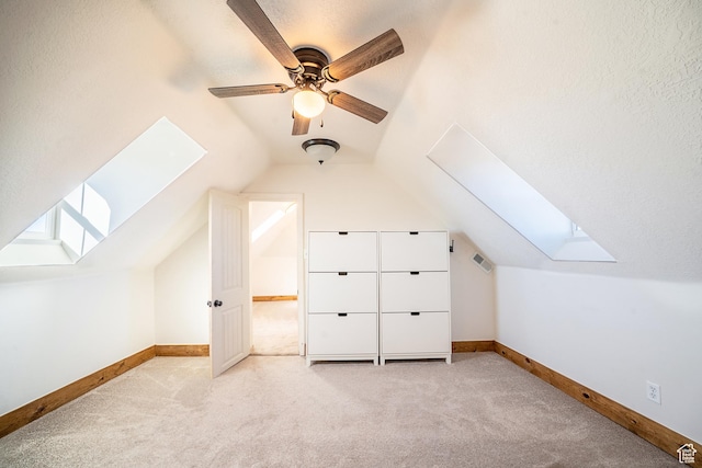 additional living space featuring light carpet, lofted ceiling with skylight, baseboards, and a textured ceiling