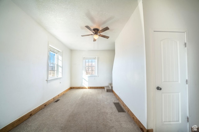 carpeted empty room with baseboards, visible vents, and a textured ceiling