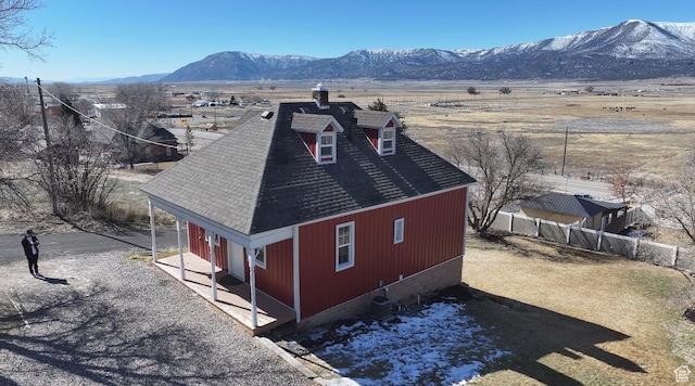 exterior space with fence, a mountain view, and roof with shingles