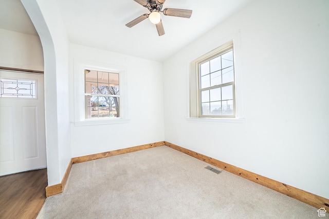 empty room with baseboards, visible vents, arched walkways, a ceiling fan, and carpet