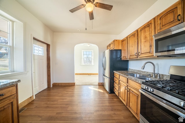 kitchen featuring dark wood-type flooring, arched walkways, stainless steel appliances, and a sink