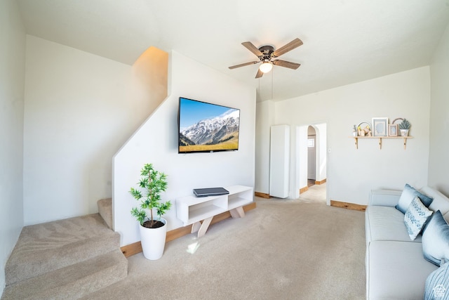 living area with baseboards, arched walkways, a ceiling fan, light colored carpet, and stairs