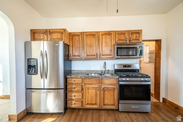 kitchen featuring brown cabinets, appliances with stainless steel finishes, arched walkways, and a sink