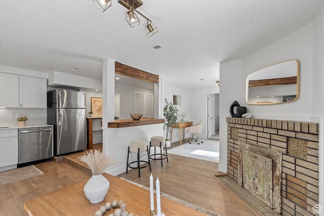 kitchen featuring appliances with stainless steel finishes, white cabinetry, light wood-style flooring, and tasteful backsplash