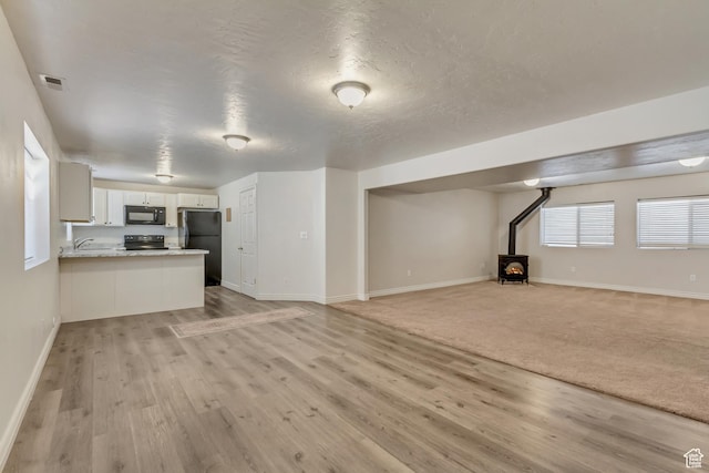 unfurnished living room with a wood stove, light wood-type flooring, visible vents, and baseboards
