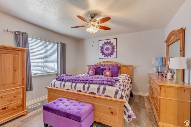 bedroom featuring light wood finished floors, visible vents, baseboards, and ceiling fan