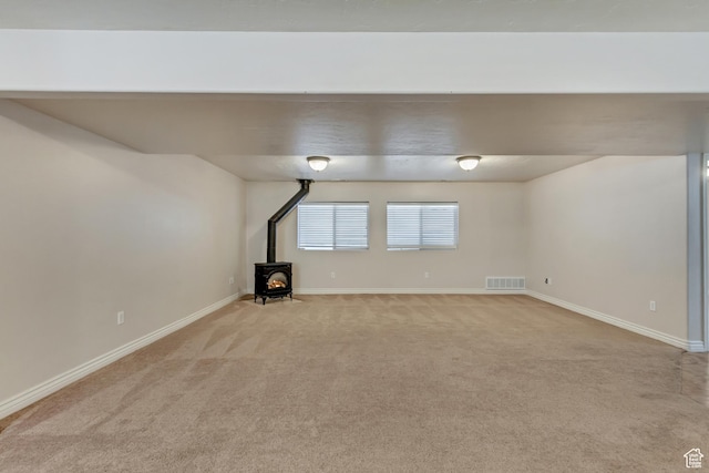 basement with a wood stove, visible vents, light carpet, and baseboards