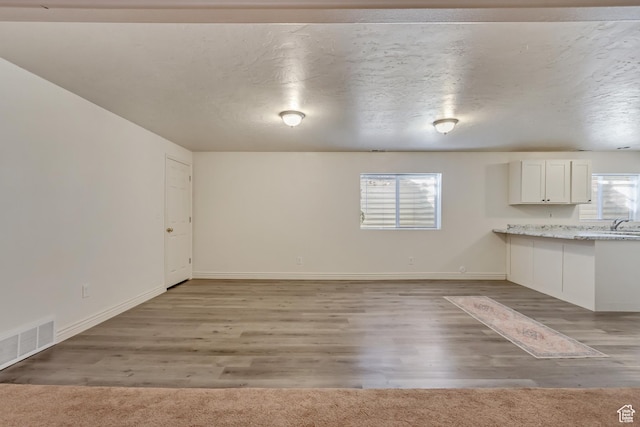 unfurnished dining area with baseboards, visible vents, light colored carpet, a textured ceiling, and light wood-style floors