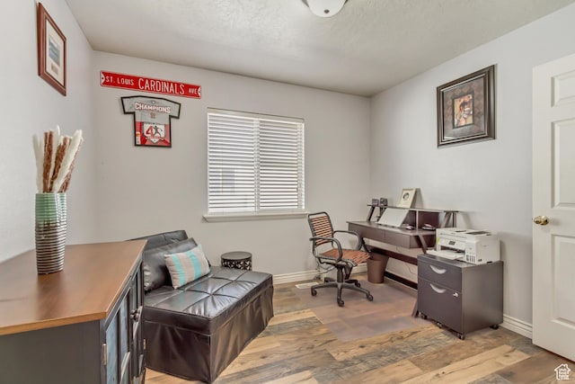 office featuring baseboards, a textured ceiling, and light wood-style floors