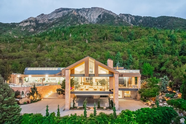 back of property featuring a balcony, a chimney, a mountain view, and a wooded view