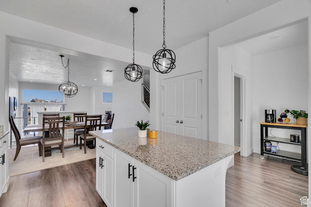 kitchen featuring light stone counters, decorative light fixtures, white cabinetry, a kitchen island, and wood finished floors