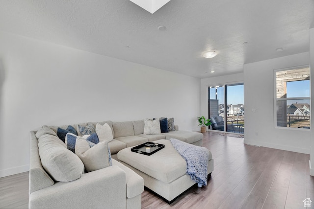 living room with a textured ceiling, a skylight, wood finished floors, and baseboards