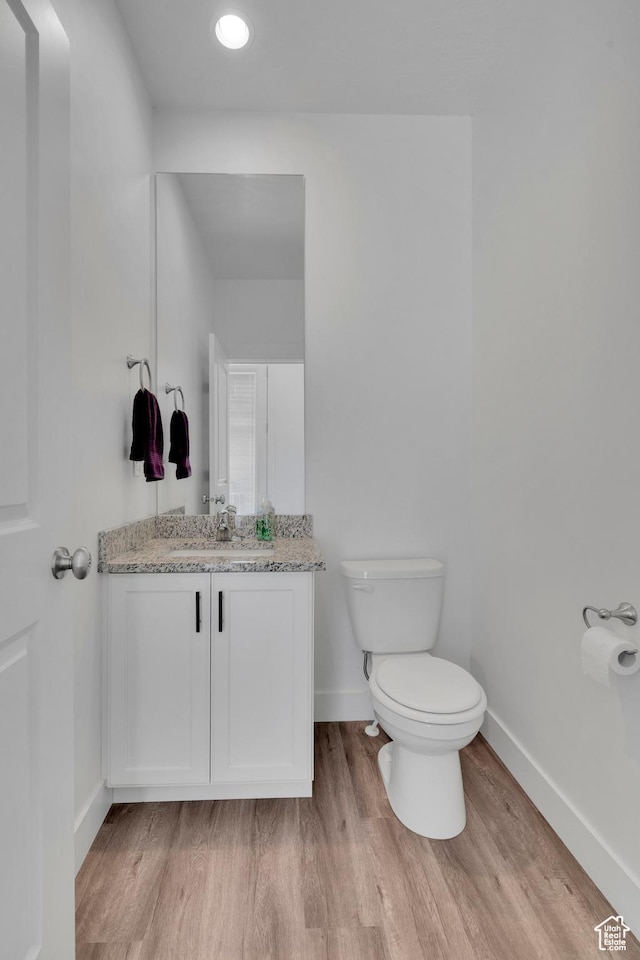 half bath with vanity, wood finished floors, toilet, and baseboards