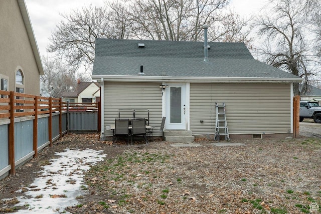 rear view of property featuring a shingled roof, entry steps, and fence