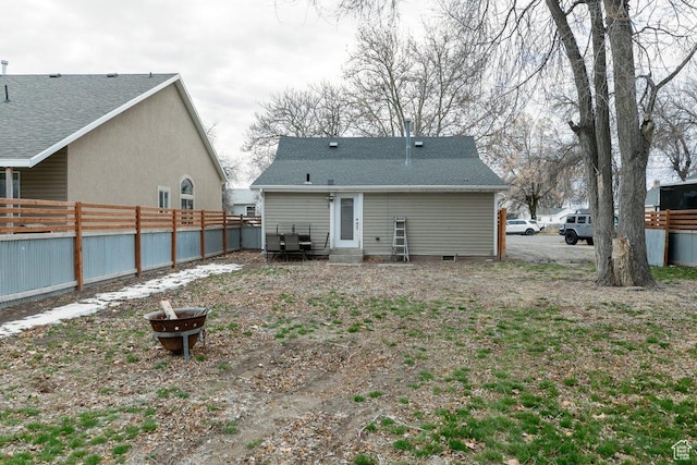 rear view of house featuring fence, a fire pit, and roof with shingles