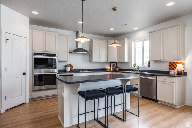 4623 N Festival Way, Eagle Mountain, UT 84005 - kitchen with dark countertops, light wood-style floors, appliances with stainless steel finishes, wall chimney range hood, and a breakfast bar area