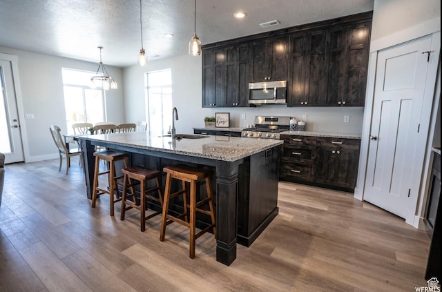3966 W 2025 S, Taylor, UT 84401 - kitchen featuring range, light wood-style flooring, stainless steel microwave, a kitchen island with sink, and a kitchen bar