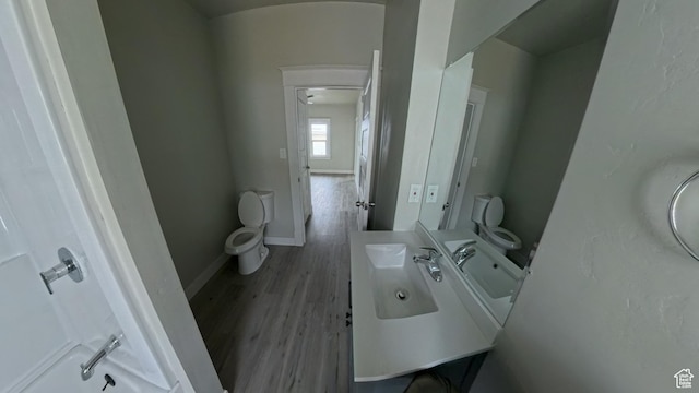 half bath with toilet, vanity, baseboards, and wood finished floors