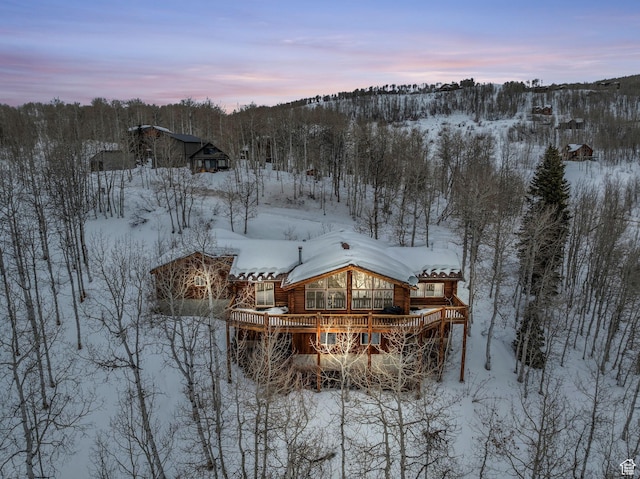 snow covered property with a wooden deck and a wooded view