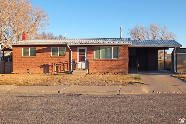 ranch-style home featuring an attached carport, concrete driveway, brick siding, and a chimney