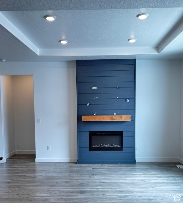 unfurnished living room with a textured ceiling, a raised ceiling, light wood-type flooring, and a large fireplace