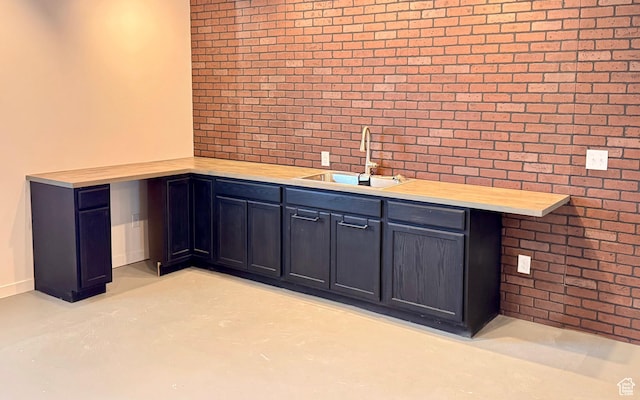 bar featuring brick wall, finished concrete flooring, baseboards, and a sink