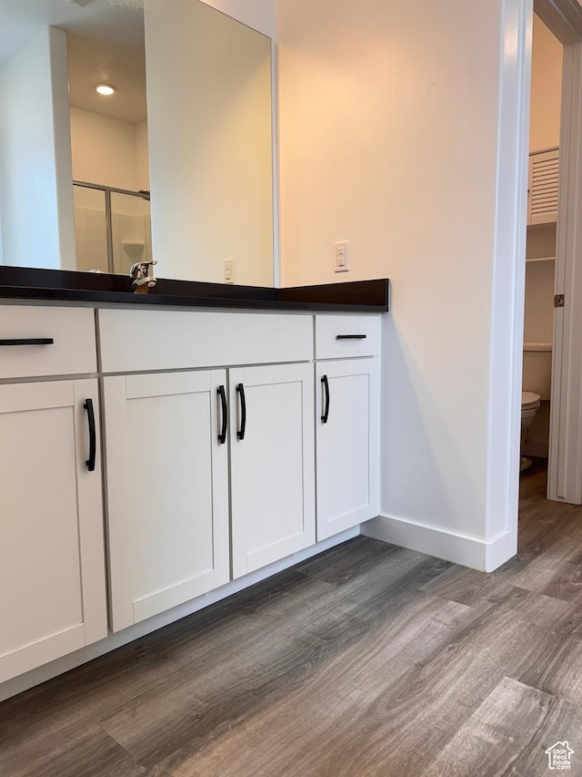 bathroom featuring vanity, wood finished floors, baseboards, a shower stall, and toilet