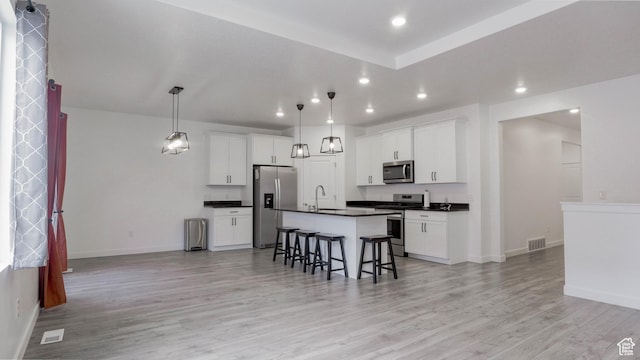 kitchen featuring visible vents, a breakfast bar, appliances with stainless steel finishes, dark countertops, and open floor plan