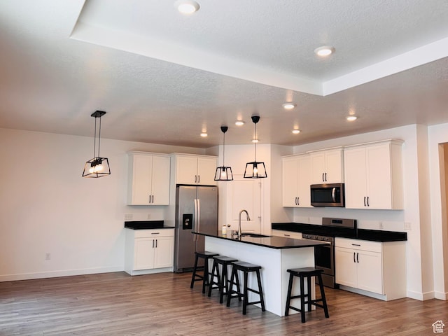 kitchen with wood finished floors, a sink, stainless steel appliances, dark countertops, and a kitchen breakfast bar