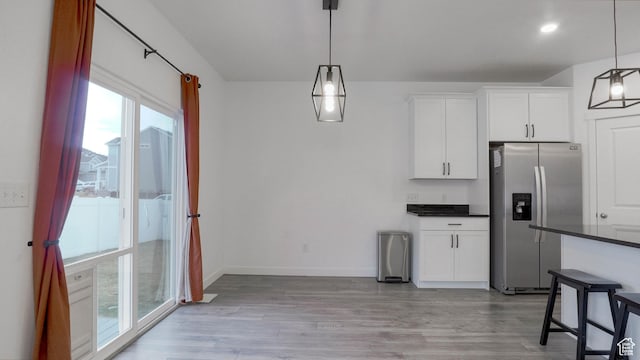 kitchen with dark countertops, baseboards, light wood-style flooring, stainless steel refrigerator with ice dispenser, and white cabinets