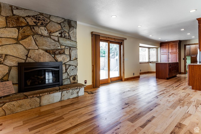 living area featuring crown molding, a stone fireplace, and light wood-style floors