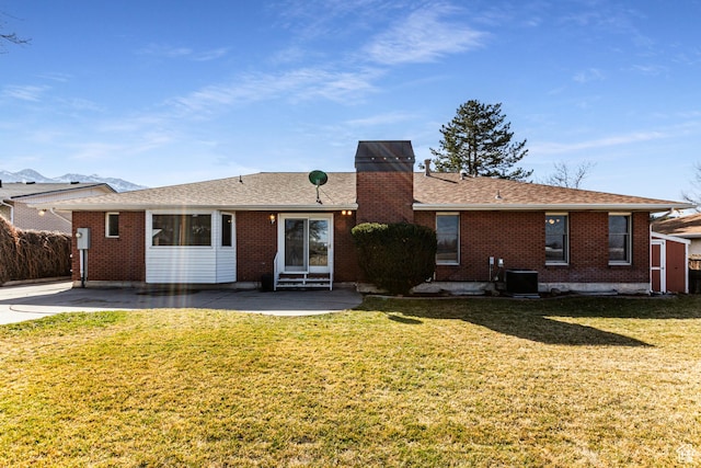 back of house featuring brick siding, a yard, a chimney, entry steps, and central AC