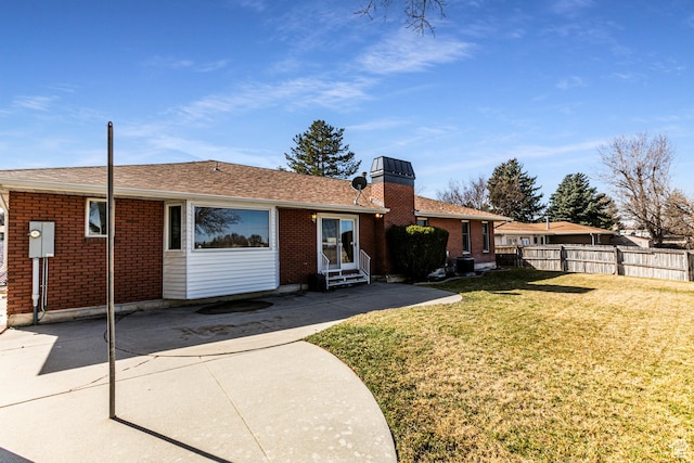 rear view of property featuring entry steps, brick siding, fence, a lawn, and a chimney