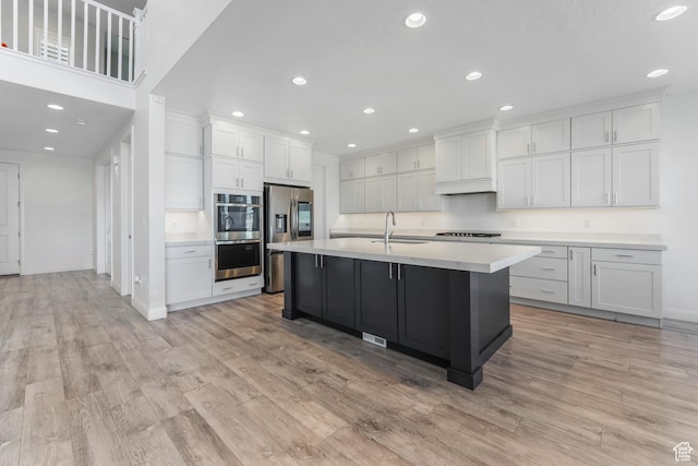 kitchen with light wood-type flooring, light countertops, appliances with stainless steel finishes, white cabinetry, and a sink