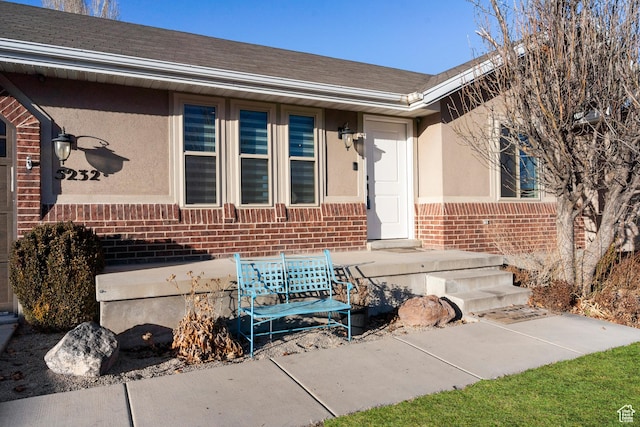 view of exterior entry featuring brick siding, a shingled roof, and stucco siding