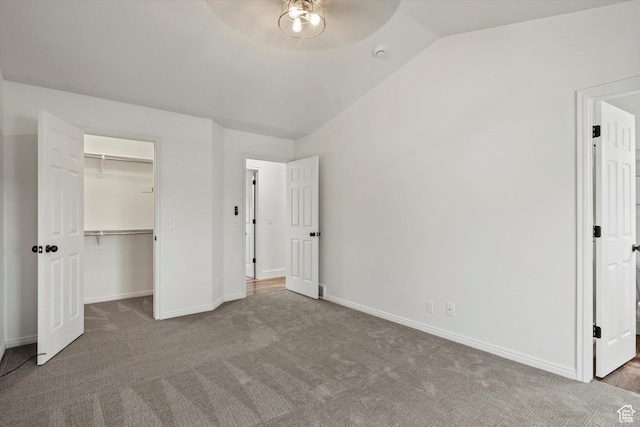 unfurnished bedroom with vaulted ceiling, baseboards, a closet, carpet floors, and a walk in closet