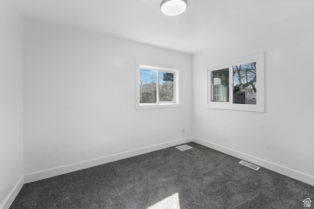 empty room with dark colored carpet, visible vents, and baseboards