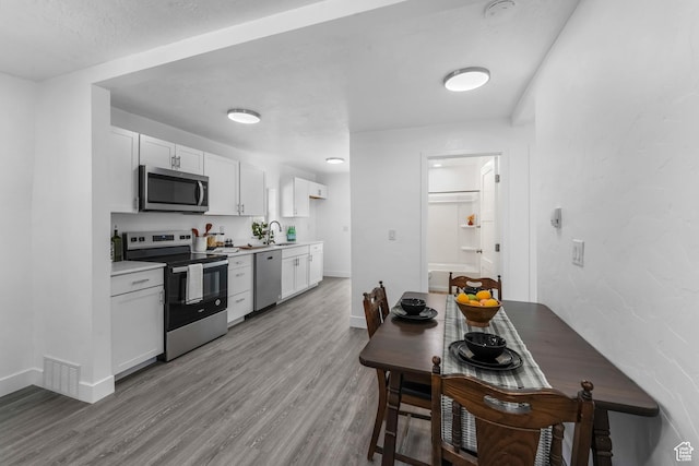 kitchen with stainless steel appliances, white cabinetry, visible vents, and light wood-style floors