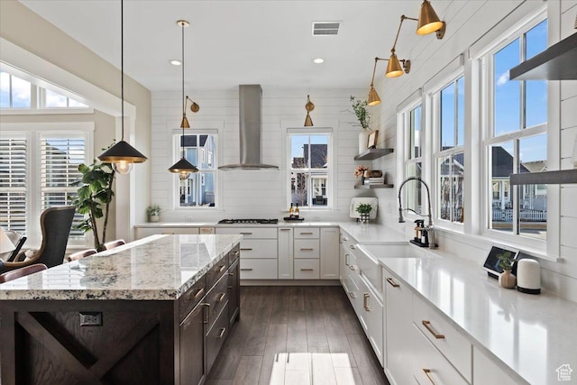 kitchen with visible vents, dark brown cabinets, wall chimney range hood, gas stovetop, and a sink