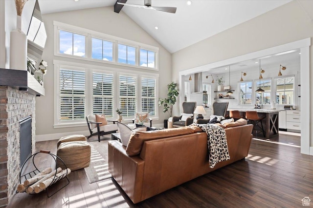 living room with baseboards, dark wood finished floors, ceiling fan, a fireplace, and high vaulted ceiling