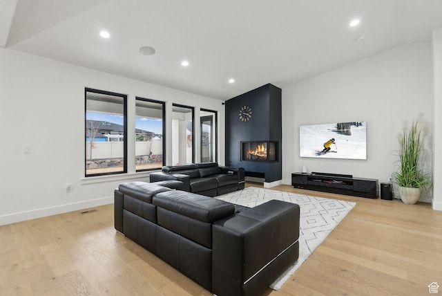 living area featuring lofted ceiling, a large fireplace, light wood-style flooring, and recessed lighting