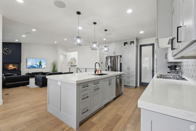 kitchen featuring appliances with stainless steel finishes, a sink, light wood finished floors, and tasteful backsplash