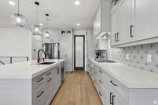 kitchen featuring light countertops, light wood-style flooring, decorative backsplash, appliances with stainless steel finishes, and a sink