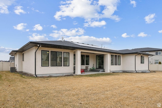 rear view of property with roof mounted solar panels, a lawn, a patio, and fence