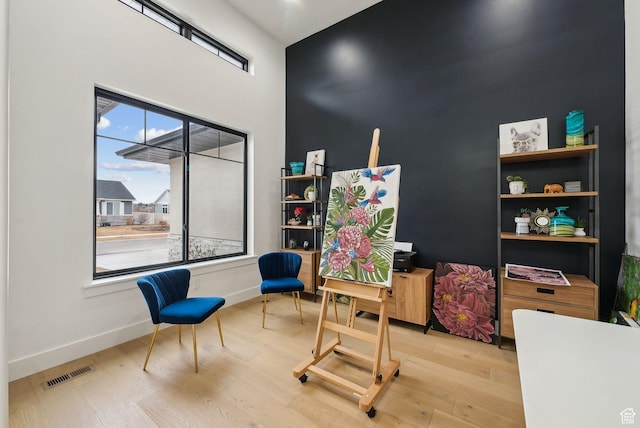 sitting room with a high ceiling, wood finished floors, visible vents, and baseboards