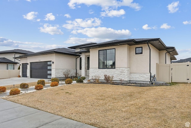 prairie-style house with stucco siding, an attached garage, a gate, fence, and stone siding