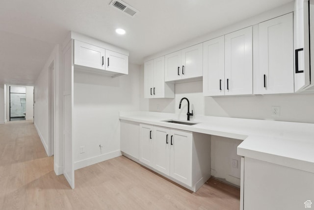 kitchen featuring light wood finished floors, visible vents, white cabinets, a sink, and baseboards